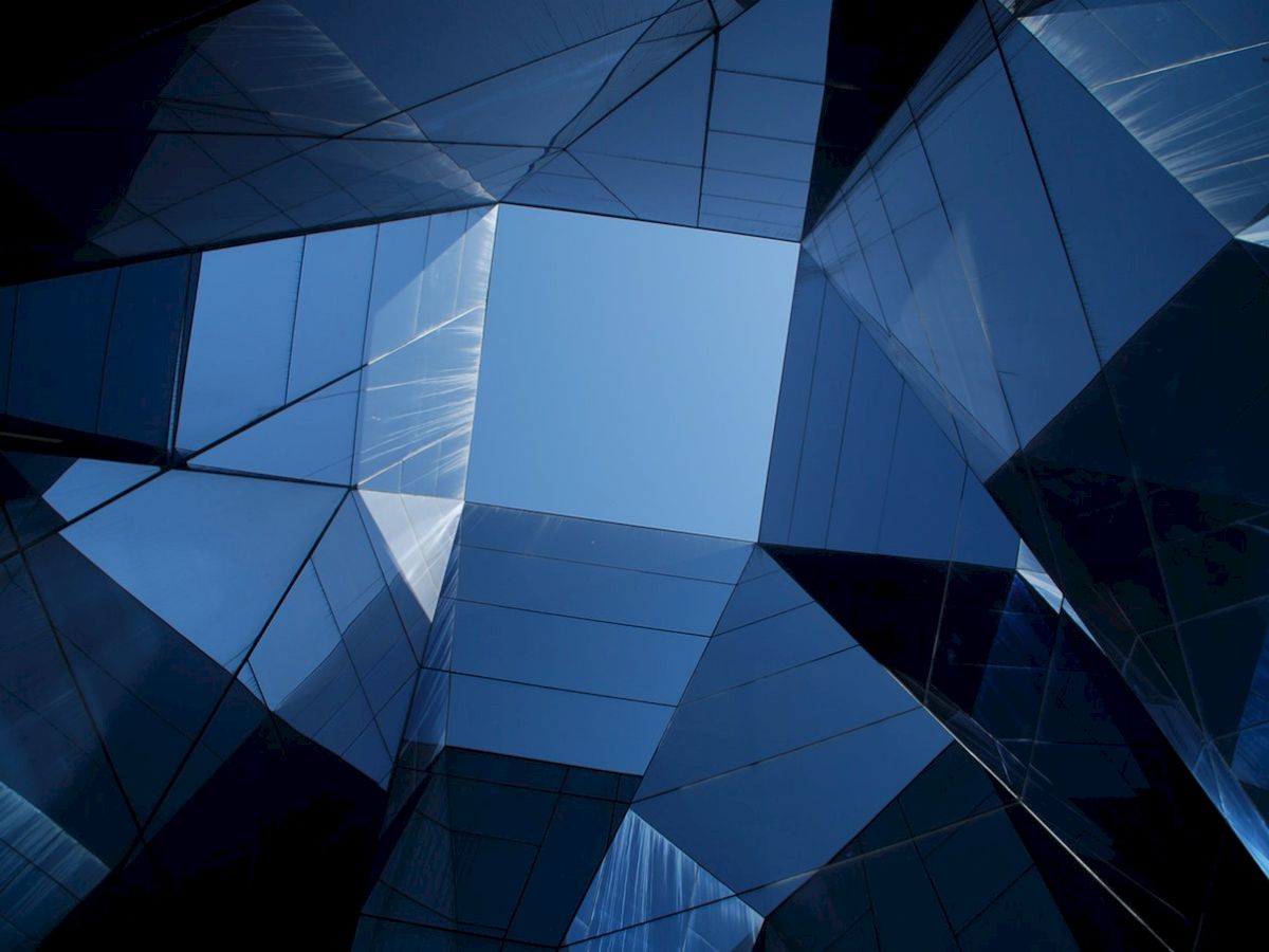The image shows a geometric pattern of reflective glass structures forming an open space through which the sky is visible.