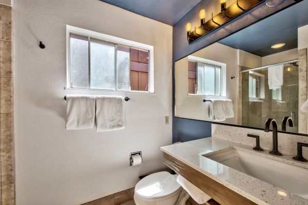 This image shows a modern bathroom with a large mirror, a vanity sink, a towel rack with two towels, a small window, and a toilet.