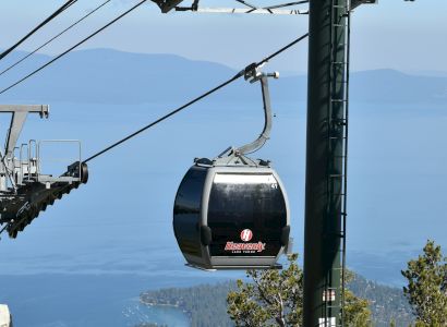 A cable car is suspended from a gondola lift system against a clear sky and mountainous backdrop, offering scenic views.
