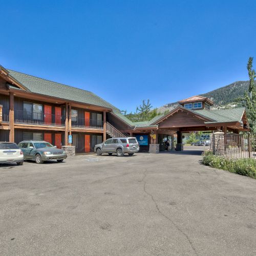 The image shows a lodge-style building with multiple vehicles parked outside, surrounded by mountains and clear skies.