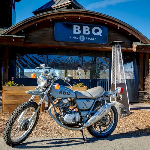 A vintage motorcycle is parked in front of a rustic building with a sign that reads 