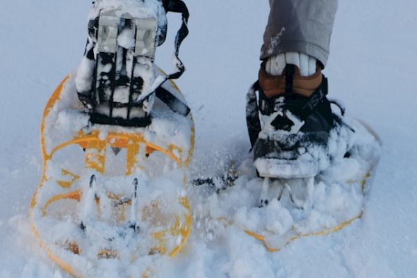 The image shows a person wearing snowshoes while walking on snow-covered ground, with their legs visible from the knee down.
