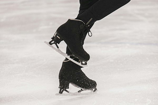A close-up image of a figure skater's legs in black skates, captured mid-spin on an ice rink.
