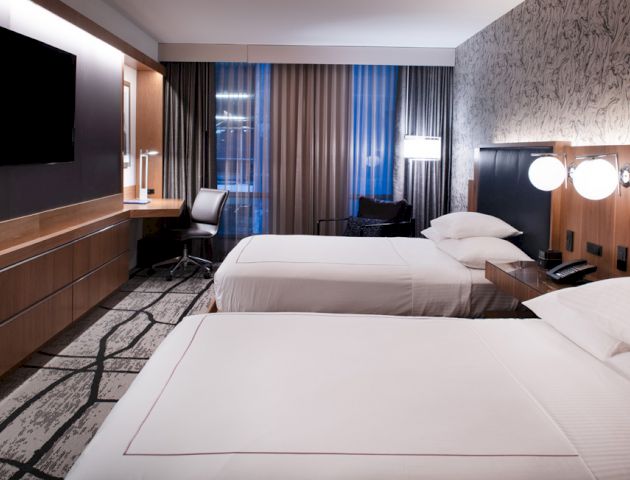 Modern hotel room with two beds, a large TV, desk, and stylish decor