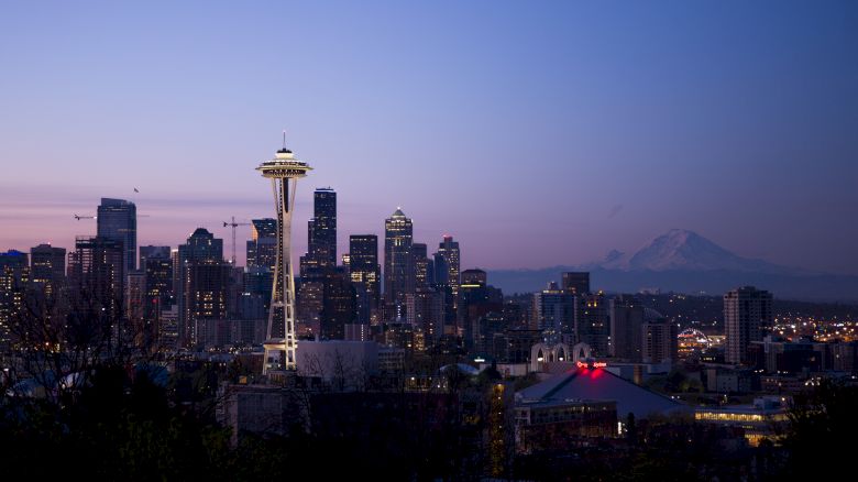 The image depicts the Seattle skyline at dusk, featuring the Space Needle and Mount Rainier in the background.